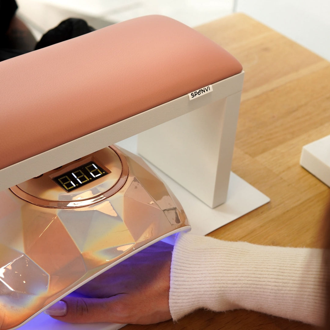 Różowa podpórka do manicure SPENVI Classic ustawiona nad lampą UV do utwardzania lakieru hybrydowego na stole w salonie kosmetycznym.