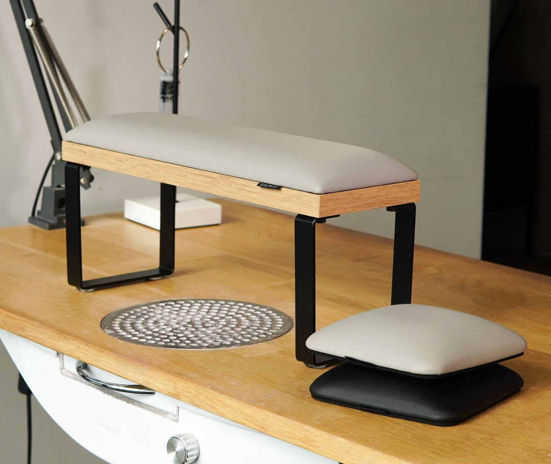 Podpórka do manicure SPENVI Loft z jasnoszarą poduszką i czarnymi metalowymi nogami ustawiona na drewnianym biurku w salonie kosmetycznym.