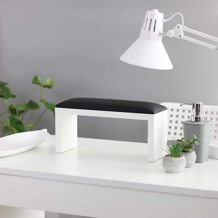 Podpórka do manicure SPENVI Classic w kolorze czarnym na białych nogach ustawiona na biurku w salonie kosmetycznym pod lampą. #kolor_black