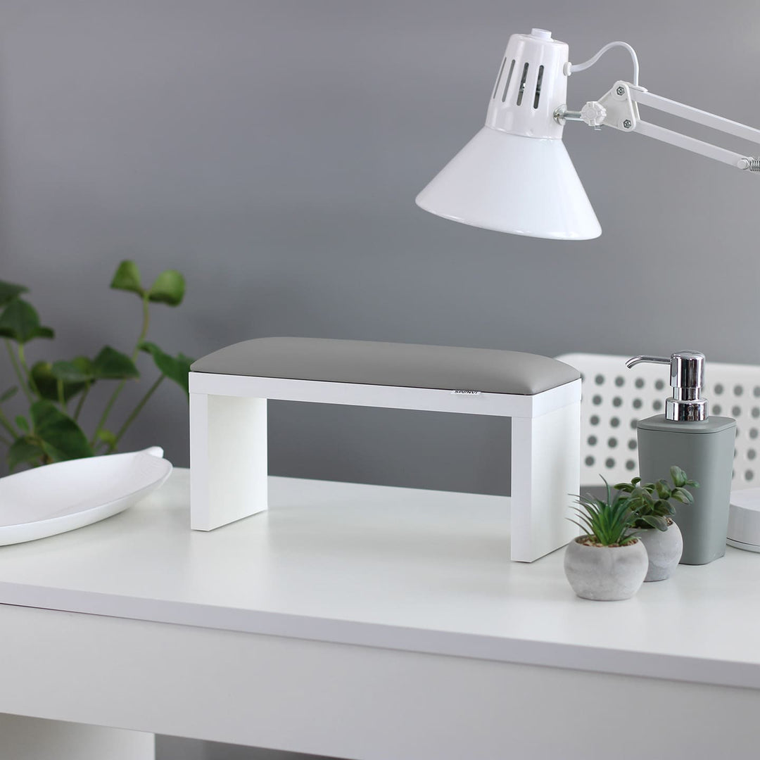 Podpórka do manicure SPENVI Classic w kolorze szarym na białych nogach ustawiona na biurku w salonie kosmetycznym pod lampą. #kolor_cloud